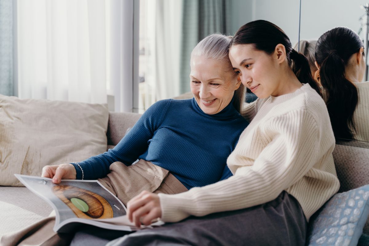 An adult daughter sitting close to her mother at home, looking through a book together